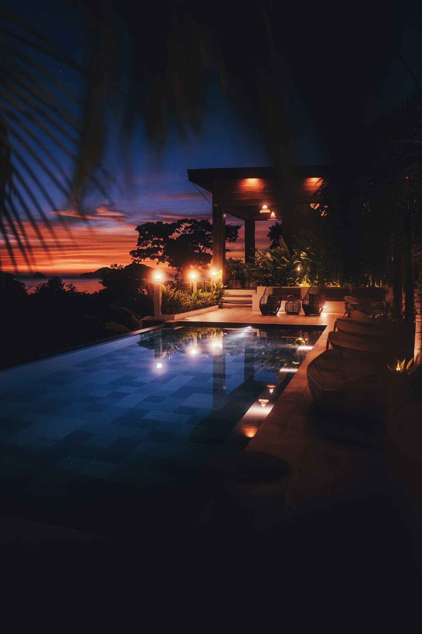 Villa pool at night with warm deck lights reflecting in the water